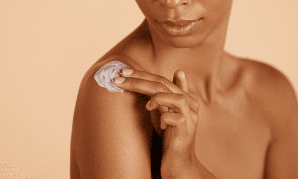 brown skin woman applying sunscreen on her shoulder