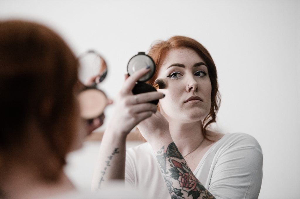 redhead applying makeup through mirror